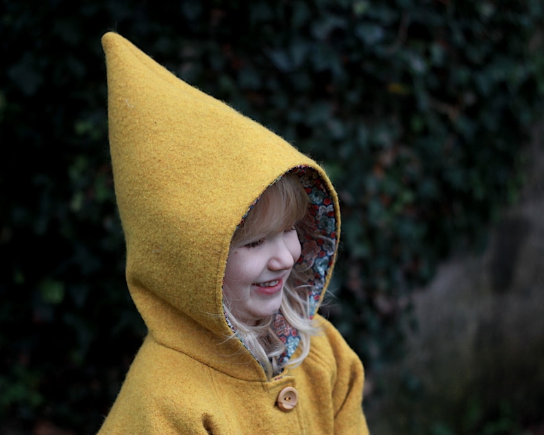 May include: A child wearing a yellow hooded coat with a floral lining. The hood is pointed and the coat has a button closure.