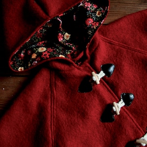 May include: A red hooded cape with a floral lining and black toggle closures.