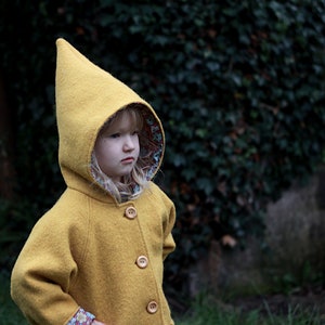 May include: A young child wearing a yellow hooded coat with a floral lining. The coat has a pointed hood and multiple buttons down the front.