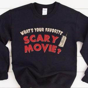 May include: Black sweatshirt with the text "WHAT'S YOUR FAVORITE SCARY MOVIE?" in a retro font, accompanied by a vintage cell phone graphic. The design is in cream and red colors.
