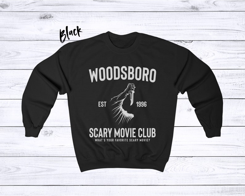 May include: Black sweatshirt with a white graphic design. The graphic features a hand holding a knife and the text "Woodsboro Est 1996 Scary Movie Club What's your favorite scary movie?"
