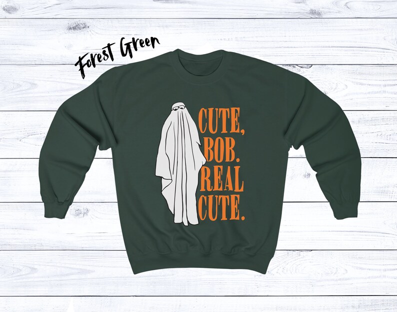 Puede incluir: Sudadera verde bosque con un gr&aacute;fico de fantasma blanco con gafas de sol. El texto "CUTE, BOB, REAL CUTE." est&aacute; impreso en naranja. Una divertida prenda de vestir con tem&aacute;tica de Halloween.