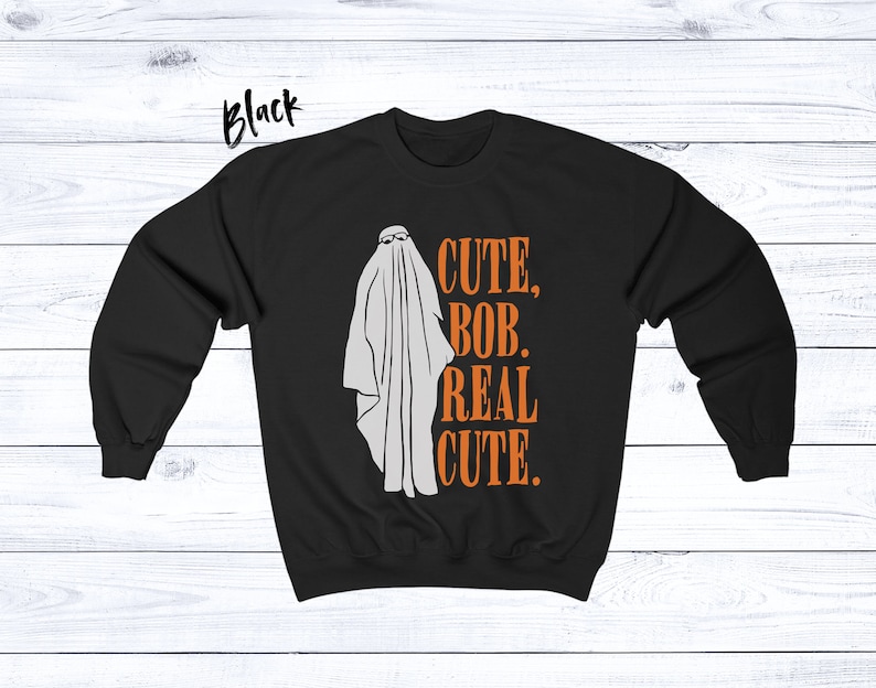 Puede incluir: Sudadera negra con un fantasma blanco con gafas de sol. El texto naranja dice "CUTE, BOB, REAL CUTE". La palabra "Black" est&aacute; escrita en la esquina superior izquierda.