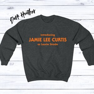 May include: Dark heather grey sweatshirt with the text "introducing JAMIE LEE CURTIS as Laurie Strode" in orange.