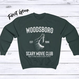 May include: Forest green sweatshirt with the text "WOODSBORO EST 1996 SCARY MOVIE CLUB WHAT'S YOUR FAVORITE SCARY MOVIE?" and a graphic of a hand holding a knife.