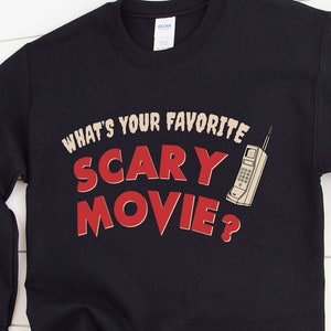 May include: A navy blue sweatshirt with the text "WHAT'S YOUR FAVORITE SCARY MOVIE?" in a retro font. A vintage cell phone graphic is to the right of the text. The sweatshirt is a Gildan brand.