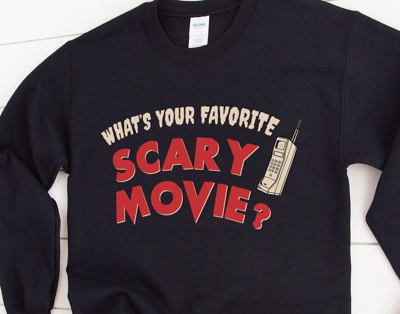 May include: A navy blue sweatshirt with the text "WHAT'S YOUR FAVORITE SCARY MOVIE?" in a retro font. A vintage cell phone graphic is to the right of the text. The sweatshirt is a Gildan brand.