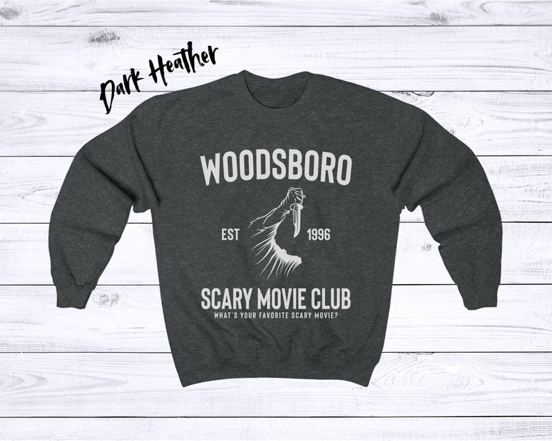 May include: Dark heather grey sweatshirt with a white graphic design. The graphic features a hand holding a knife with the text "Woodsboro Est 1996 Scary Movie Club What's your favorite scary movie?"
