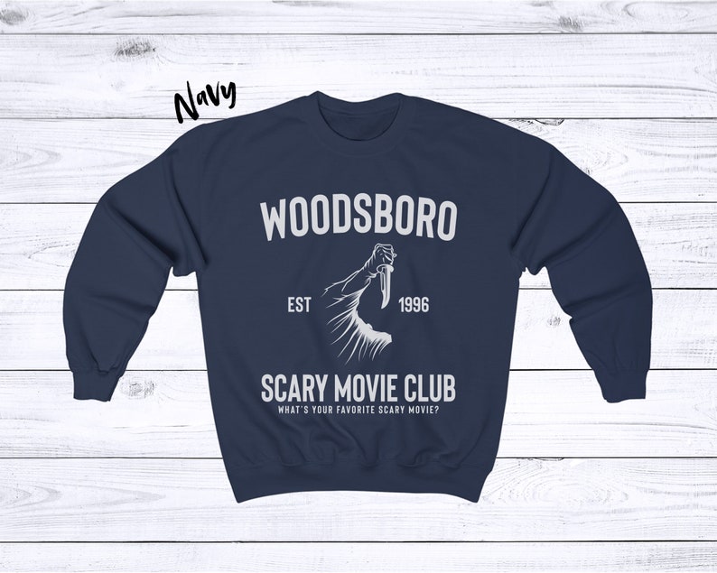 May include: Navy blue sweatshirt with a white graphic design that says "Woodsboro Est. 1996 Scary Movie Club What's your favorite scary movie?"