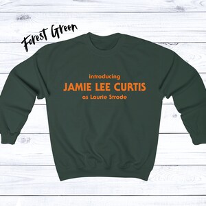 May include: Forest green sweatshirt with the text "introducing JAMIE LEE CURTIS as Laurie Strode" in orange.