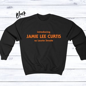 May include: Black sweatshirt with orange text that reads "introducing JAMIE LEE CURTIS as Laurie Strode".
