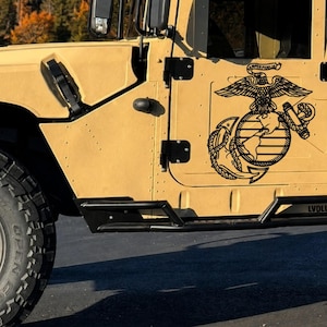 May include: A tan-colored vehicle featuring a black United States Marine Corps Eagle, Globe, and Anchor emblem decal on the side door. The emblem includes the text Semper Fidelis above the eagle. A black metal side step is mounted below the door.