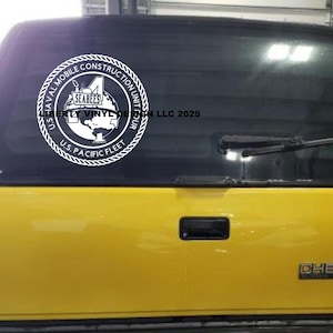 May include: A white vinyl decal featuring the U.S. Naval Mobile Construction Unit 4, Seabees, and U.S. Pacific Fleet emblem. The decal is on the rear window of a yellow Chevrolet truck. The text "Liberty Vinyl Design LLC 2025" is also visible.