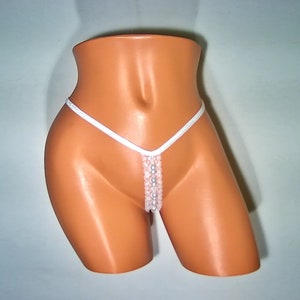 May include: White lingerie with a delicate lace design and pearl accents. The lingerie has a string tie design and is shown on a mannequin.