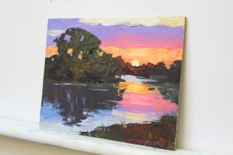 May include: Oil painting of a sunset over a river. The sky transitions from purple to orange, reflecting in the water. Dark green trees line the riverbank, with brushstrokes creating texture and depth. The artwork is on a wooden panel.