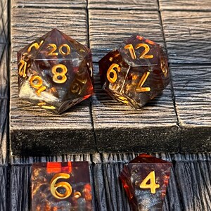 May include: Four polyhedral dice with gold numbers on a brown wooden background. The dice are a 20-sided die, a 12-sided die, a 6-sided die, and a 4-sided die. The dice are translucent and have a speckled appearance.