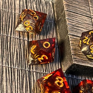 May include: Six amber-colored dice with gold numbers. The dice are on a wooden surface with a brown and black pattern.