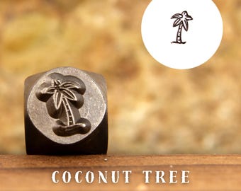 May include: A metal stamp with a design of a coconut tree. The stamp is on a wooden surface with the text "COCONUT TREE" below it.