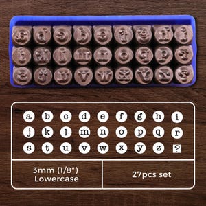 Pode incluir: Um conjunto de 27 carimbos de letras minúsculas em uma bandeja de plástico azul. Os carimbos medem 3 mm (1/8 de polegada) e estão dispostos em ordem alfabética. Os carimbos são feitos de metal e têm um acabamento preto.