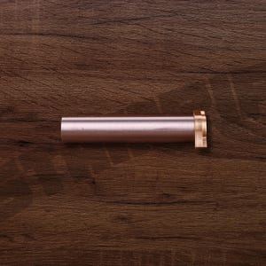 K&ouml;nnte beinhalten: Ein zylindrisches Metallobjekt in Ros&eacute;gold mit einem messingfarbenen Flansch an einem Ende. Das Objekt liegt horizontal auf einer dunkelbraunen Holzoberfl&auml;che. Das Objekt scheint eine Komponente oder ein Teil eines gr&ouml;&szlig;eren Artikels zu sein.