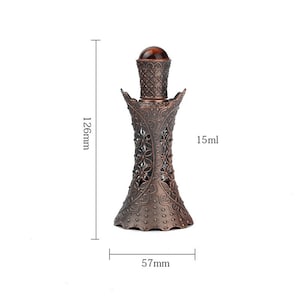 K&ouml;nnte beinhalten: Eine bronzefarbene Parf&uuml;mflasche mit floralem Design. Die Flasche ist 12,6 cm hoch und 5,7 cm breit, mit einem Fassungsverm&ouml;gen von 15 ml. Die Flasche hat ein detailliertes Filigranmuster und einen dunkelbraunen Verschluss.