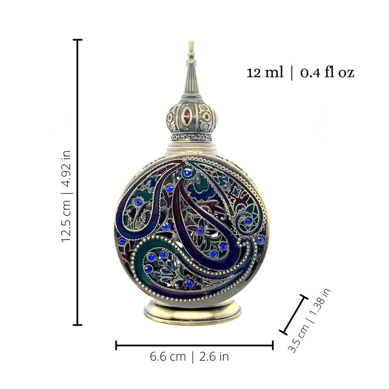 K&ouml;nnte beinhalten: Eine verzierte Parf&uuml;mflasche mit einem silberfarbenen Metallsockel und -verschluss. Die Flasche ist 12,5 cm hoch und 6,6 cm breit, mit einem Fassungsverm&ouml;gen von 12 ml. Der K&ouml;rper weist ein Paisley-Design in Blau-, Gr&uuml;n- und Lilat&ouml;nen auf, akzentuiert mit blauen Edelsteinen.