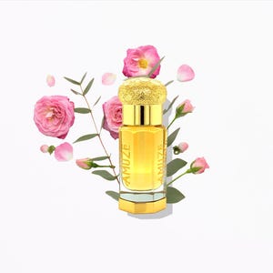 May include: A gold-colored perfume bottle with the word "AMUZE" printed on the front. The bottle is surrounded by pink roses, rosebuds, and green leaves, set against a white background. The bottle has a decorative gold cap.