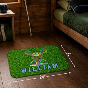 May include: A rectangular bath mat with a green grass design and a lacrosse graphic in multiple colors. The mat is 24 inches long and 17 inches wide, with the name "WILLIAM" printed in blue. The text "BATH MAT" is at the top.