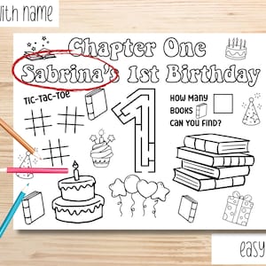 May include: A black and white printable colouring page for a first birthday, with the text "Chapter One Sabrina's 1st Birthday". Includes a tic-tac-toe game, a maze, and illustrations of books, a cake, and balloons. Colouring pencils are scattered around.