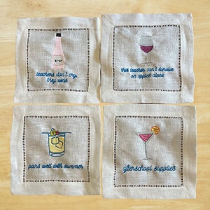 以下が含まれることがあります： 刺繍された飲み物のイラストと、教師をテーマにしたユーモラスな言葉が書かれたリネン製のカクテルナプキン4枚セット。言葉は「先生は泣かない、ワインを飲む」「この先生はリンゴだけでは生きられない」「夏によく合う」「放課後の備品」です。