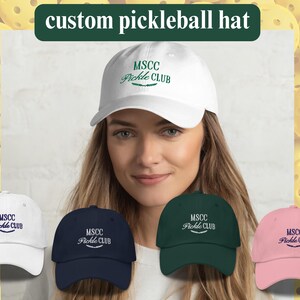 Pu&ograve; includere: Cinque cappellini da pickleball di diversi colori con il testo "MSCC Pickle Club" ricamato sul davanti. I cappellini sono bianchi, blu navy, verdi, rosa e neri.