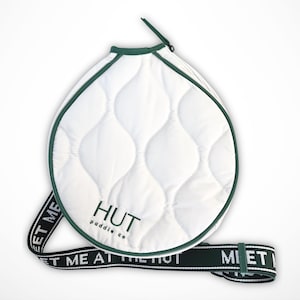 May include: White quilted paddle bag with a green zipper and a green strap that says "Meet me at the Hut Paddle Co."