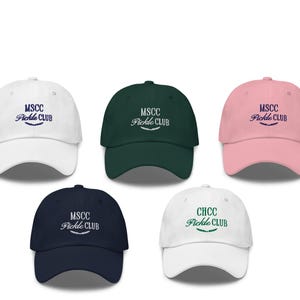 Pu&ograve; includere: Cinque cappellini da baseball di diversi colori con testo ricamato. I cappellini sono bianchi, verdi, rosa, blu scuro e bianchi con testo verde. Il testo sui cappellini recita "MSCC Pickle Club" e "CHCC Pickle Club".