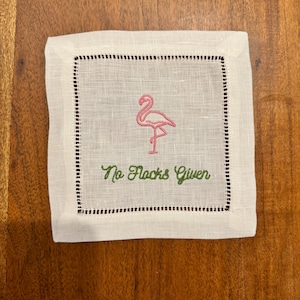 May include: White linen cocktail napkin with a pink flamingo and the text "No Flocks Given" embroidered in green thread.