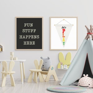 May include: A playroom with a white wall, a wooden table and chairs, a teepee tent, and two framed prints. One print says "Fun Stuff Happens Here" and the other has a white pennant with the words "Let's Play" in rainbow colors.