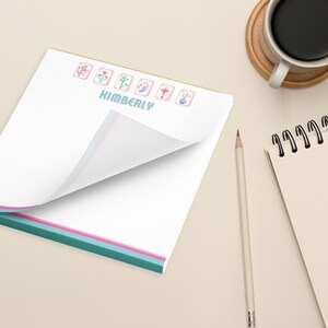 May include: A white notepad with a teal, pink, and white border. The notepad has a personalized name, "KIMBERLY", and a row of colorful Chinese mahjong tiles at the top.