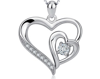 May include: Silver necklace featuring a double heart pendant. The larger heart encloses a smaller heart with a single clear stone at its centre. The larger heart is adorned with a row of small clear stones.