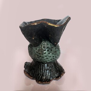 May include: A unique, handcrafted ceramic vase with a dark teal exterior and bronze accents. The vase features a textured, bulbous midsection and a flared, ruffled base. The rim has a wavy, organic shape.