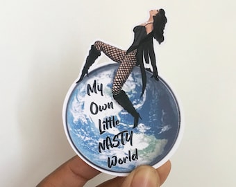 May include: A sticker featuring a woman in a black outfit sitting on a globe with the text "My Own Little Nasty World" printed on it.