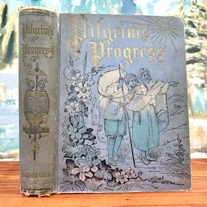 May include: A vintage, illustrated book titled "Pilgrim's Progress" with a blue cover and gold lettering. The cover features a scene of two figures walking through a forest with a large bag on their backs.