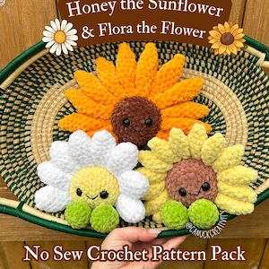 May include: Three plush crochet flowers with smiling faces and black eyes. One large yellow sunflower, one white daisy, and one smaller yellow flower, each with green feet. Text reads: Honey the Sunflower & Flora the Flower No Sew Crochet Pattern Pack.