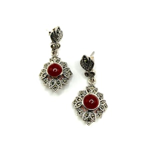 A pair of silver earrings with red carnelian centers and marcasite accents, hanging on a white background.