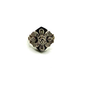 A silver ring with a black onyx center and marcasite accents forming a floral design, viewed from the top on a white background.