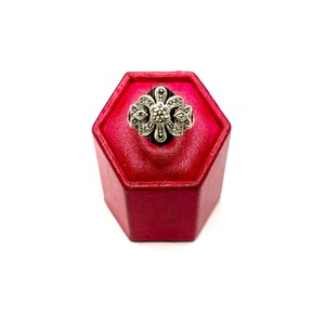 A silver ring with a black onyx center and marcasite floral design, displayed on a red hexagonal ring stand, viewed from the top.