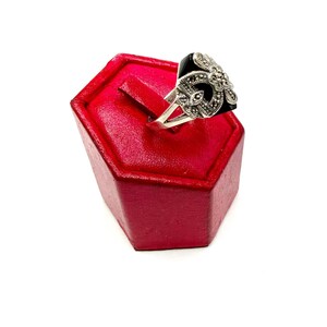 A silver ring with a black onyx center and marcasite floral design, displayed on a red hexagonal ring stand, viewed from the side.