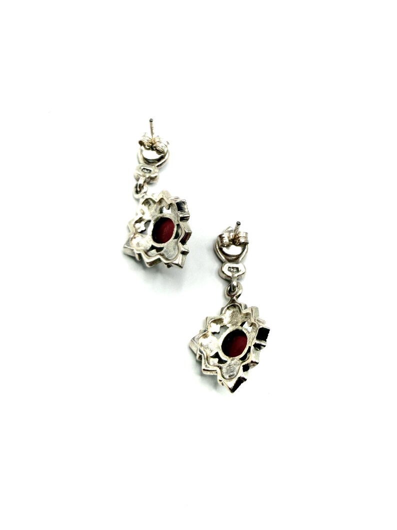 The back view of two silver earrings with red carnelian centers and marcasite accents, showing the posts and clasps on a white background.