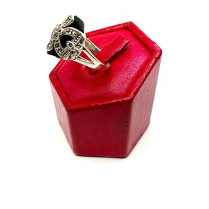 A silver ring with a black onyx center and marcasite floral design, displayed on a red hexagonal ring stand, viewed from a different side angle.