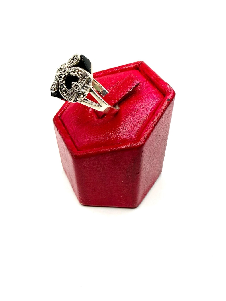 A silver ring with a black onyx center and marcasite floral design, displayed on a red hexagonal ring stand, viewed from a different side angle.