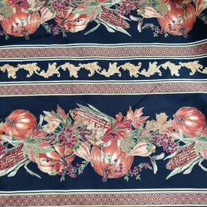 May include: Black fabric with a repeating autumn-themed pattern. The design features pumpkins, corn, berries, and fall leaves in shades of orange, red, and green. Decorative gold and brown borders complete the design.