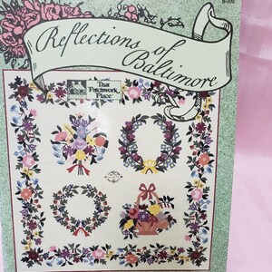 May include: A book cover titled "Reflections of Baltimore" featuring floral designs. The cover has a green border and a banner with the title. The designs include floral bouquets, wreaths, and a basket of flowers. The author's name, Jeana Kimball, is at the bottom.